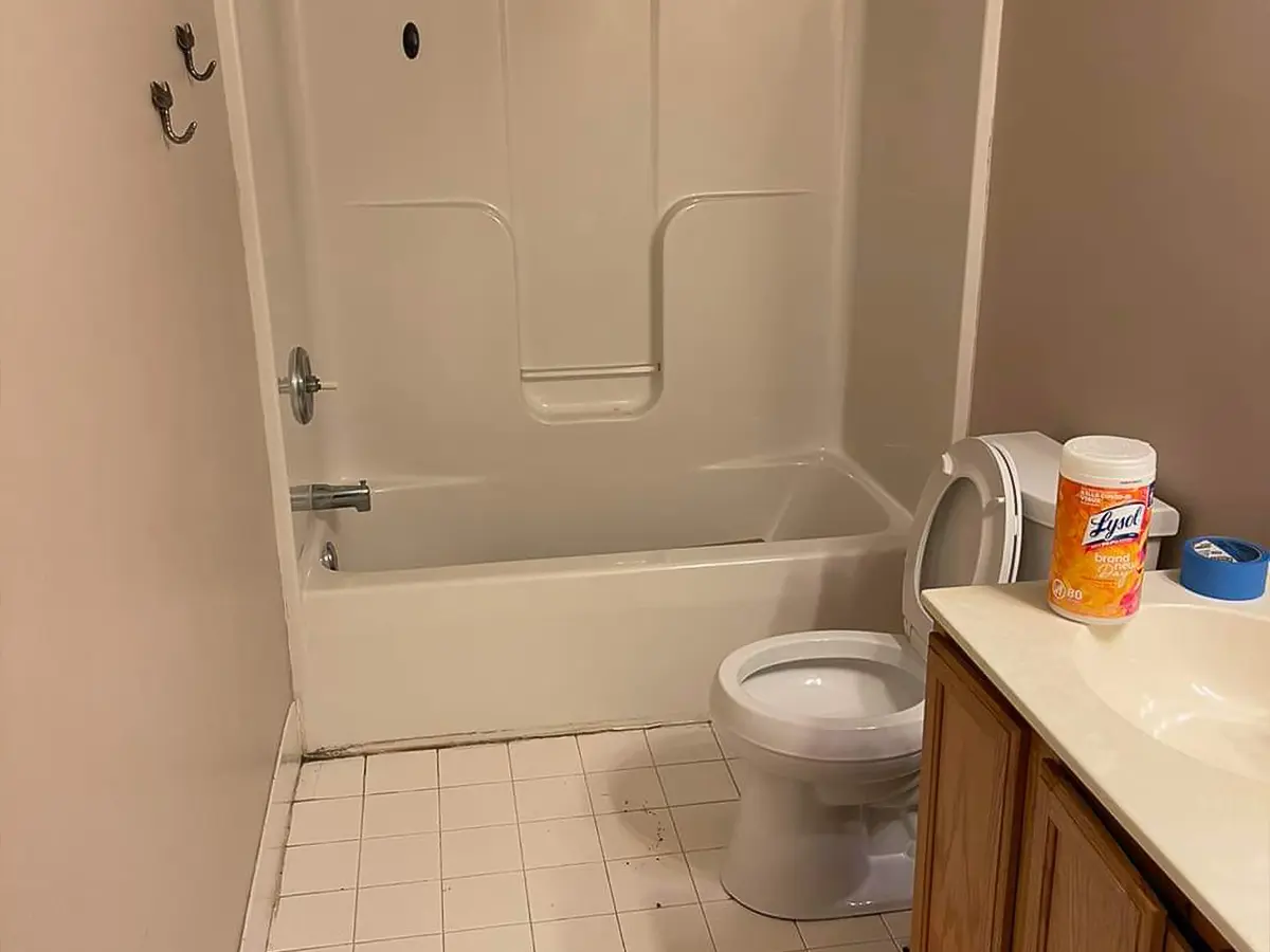 Before bathroom remodel showing basic tub and outdated tile flooring.