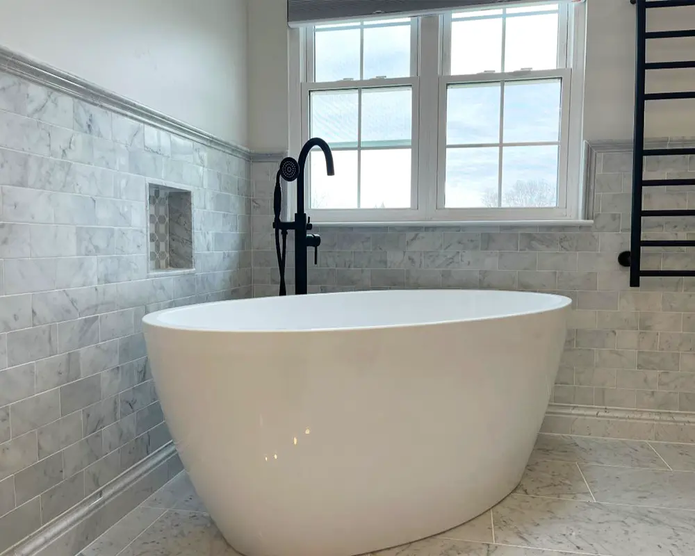 Luxurious freestanding bathtub with black matte faucet and marble tile backdrop.