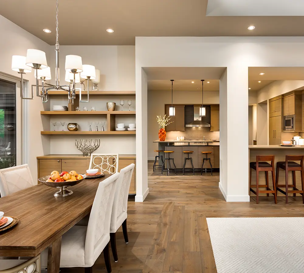 Open-concept dining room and kitchen with neutral colors, sleek lighting, and wooden furniture for a warm ambiance.