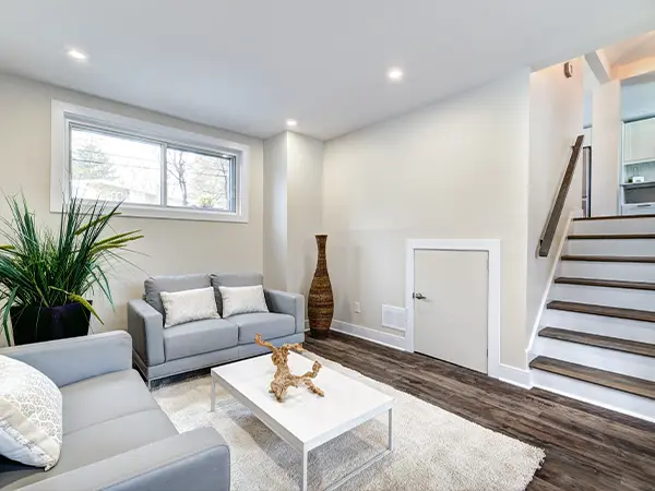 Modern basement living room with white walls, hardwood floors, and stylish gray furniture.