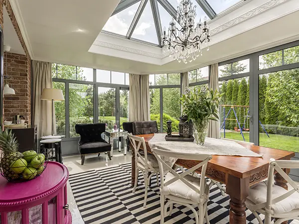 Elegant sunroom featuring large skylights, a chandelier, and a view of a lush backyard garden.